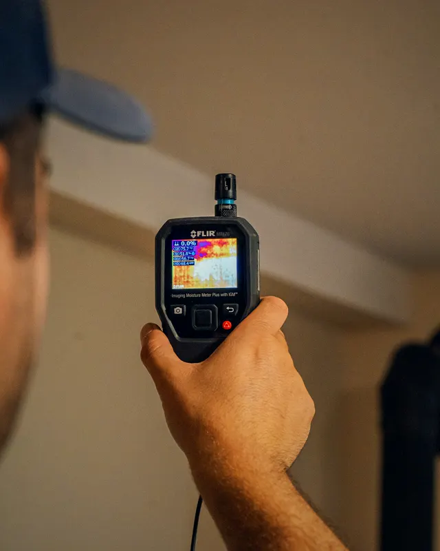 Handheld FLIR thermal camera, its screen showing a false-colour image.